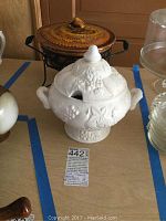 White ceramic gravy bowl with fruit relief design and matching lid with a pointed knob handle.