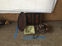 Shot of electric water fountain, two wall decor panels, metal tray, and carved wooden leaf tray on carpet under window