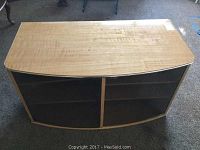 Wood and glass TV stand with curved front and two glass doors closed, showing wood surface and shelving inside.