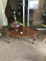 Coffee table shown from an angle on carpet with the glass lamp placed on top; visible scratches on wood surface.