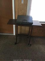 Full view of typewriter placed on wooden table with fold-out sides, showing general size and condition of both items.