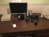 Dell computer monitor with office supplies including staplers, mouse, tape dispenser, and external drive on wooden desk.