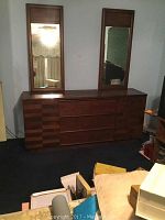 Full view of the dresser with two mirrors on top in a room with dark carpet and various items around.