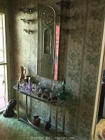 Photo showing full setup of mirror clock above glass console table with brass legs, small glass and ceramic decor on and under the table, bust sculptures on floor.