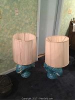 Two blue elephant base table lamps with white fabric shades on dark blue carpet against a mottled greenish wall.