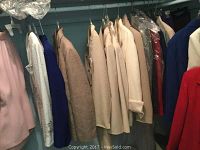 Photo showing a variety of ladies suit jackets in colors including pink, white, beige, and blue, hung on a rack.