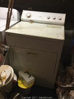 Front and top view of white Whirlpool electric clothes dryer with visible rust and dirt on top surface. Control panel features cycle selector dial and temperature settings.