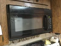Front view of black over-the-stove microwave oven showing glass door with mesh screen and black handle mounted above stove area.