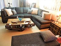 Three-piece grey sectional sofa in L-shape with throw cushions and storage ottoman in background