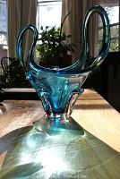 Blue Murano glass bowl with curved handles and feet, shown in sunlight highlighting translucency and blue hues