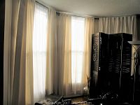 Full corner installation showing cream drapes and white sheers on double rods