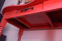 Close-up of the underside showing table's structural support and turned legs painted red.