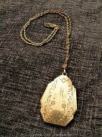 Front view of locket showing floral engraving and initial 'M'