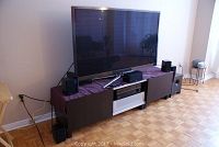 Front view of Samsung 59" TV on stand with connected speakers and cables