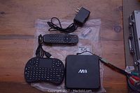 Full lot image showing IPTV box, wireless keyboard remote, standard remote, power adapter, and a small AV cable in plastic.