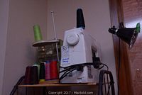 White Kenmore sewing machine on wheeled stand with multiple thread spools at front