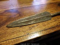 Close-up of spearhead showing metal with central ridge and aged patina.