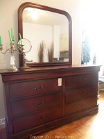 Full view of wooden dresser with six drawers and framed mirror atop it in a room setting.