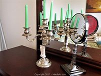 Silver-plated 5-arm candelabra with green candles and vanity mirror reflecting both items on wooden surface.