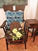 Wooden chair with armrests, blue cushion on backrest, small wooden side table beside it, and decorative items on seat including yellow artificial flowers and a large wooden button shape.