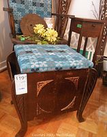Wooden magazine rack with padded lid and carved decoration seen frontally with other furniture in background