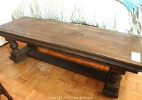Full view of rustic wooden coffee table with dark finish and decorative edges showing front and top surfaces, along with parquet floor beneath.