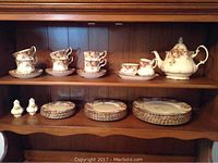 Full display of china set on wooden shelf including cups, saucers, plates, teapot, creamer, sugar bowl, salt and pepper shakers