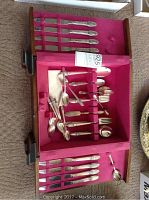 Full view of standing wooden canteen open showing the flatware collection arranged inside on pink lining.