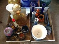 Top view of multiple vases, glassware, candle holders, and a large amber glass decanter with stopper grouped in two cardboard trays.