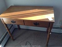 Front view of the maple desk showing drawer and turned legs.