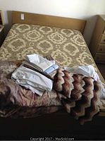 Full view of double bed with mattress, box spring, and assorted bed linens including two knitted blankets.