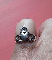 Close-up photo of sterling silver Celtic Claddagh ring worn on finger showing heart, crown, and hands design.
