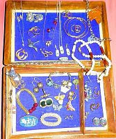 Photo showing the open wooden box with jewelry displayed on purple felt, including earrings, necklaces, rings, bracelets, pins, and aluminum cat figure.