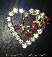 Close-up of the heart shaped brooch showing clear rhinestones and ruby colored synthetic stones on a gold-tone metal base.