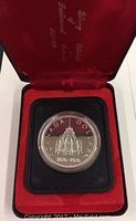 Front side of the 1976 Canadian silver dollar showing the Parliamentary Library building and dates 1876-1976, displayed in a red velvet box.