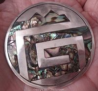 Front view of round sterling silver brooch with abalone inlay, showing abstract geometric pattern.