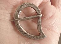 Front view of the Celtic sterling silver pin showing leafy and floral engravings and the overall shape and design held in a hand for size reference.