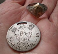 Coin and ring held in palm, showing detailed engravings on coin with maple leaf and text 'FRANCE 1916-19', and ring face with '14 guerre 18' engraving.