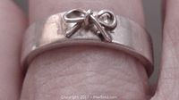 Close-up front photo of silver ring showing bow detail on band.