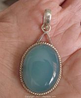 Front view of sterling silver pendant showing twisted rope frame around translucent blue oval agate cabochon stone, held in hand for scale.