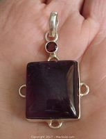 Front view showing deep red round garnet above bezel-set square purple amethyst in sterling silver setting held in hand for size reference.