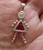 Front view of a sterling silver girl-shaped pendant with red triangular center stone and clear round head stone, held in hand showing scale.