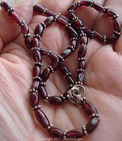 Close-up view of garnet beads with silver spacer beads and silver clasp on necklace held in hand.