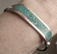 Silver bangle with malachite chip inlay worn on wrist showing curved design and clasp.