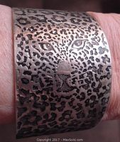 Close-up frontal view showing detailed feline face with textured and darkened spots on metal bangle bracelet.
