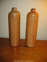 Two tall stoneware wine bottles standing side by side, showing their length and shape.