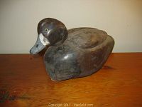 Front side view of the hand carved wooden duck decoy showing head, glass eye and painted feather details