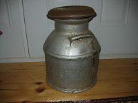 Front view of vintage cream can showing attached lid and metal handles with rust spots.