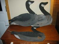 Three hand-painted Canada Goose folk art silhouettes arranged on a wooden surface, showing full body including metal rods for ground placement.