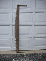 Full view of the old two-man crosscut saw leaning against a garage door showing the long metal blade with large teeth and a wooden handle at each end.